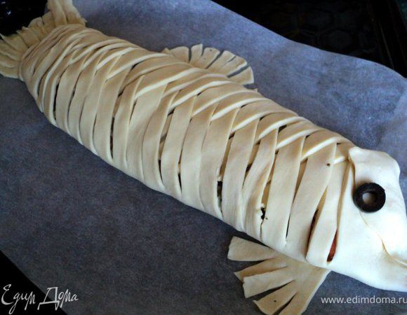 Закрыть начинку полосками теста в виде плетенки, сформировать головку и хвост из краев теста в торцах, Из остатков теста сделать плавники. Глаз сделать из колечка оливки.
