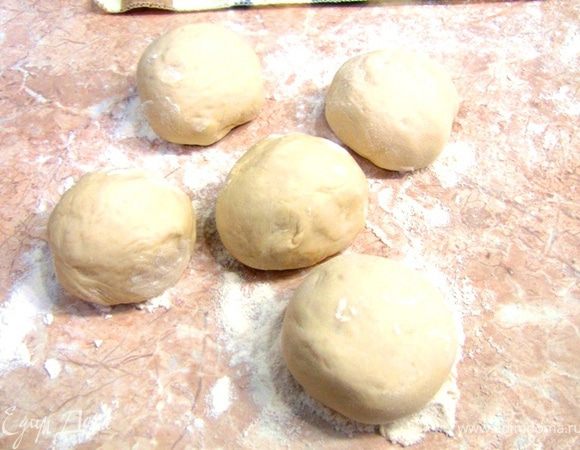 После этого посыпьте стол мукой и выложите тесто на стол и порежьте его на равные куски весом около 80 грамм. Учитывая, что теста у вас получается около полутора килограмм, должно получиться около 20 кусков.
Накройте куски, с которыми вы не работаете в настоящий момент, чтобы они не высохли.
Возьмите один кусок теста. Выбейте из него воздух (можно прямо кулаком несколько раз).
Скатайте из него шар, как вы скатываете тефтели.