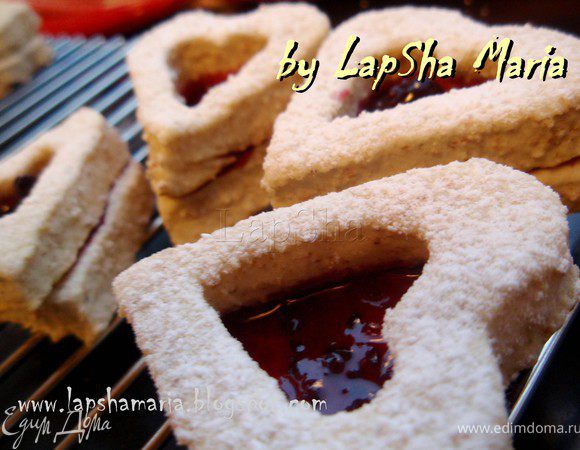 Выложить печенье на решетку и дать немного остыть. Затем на цельные сердечки тонким слоем намазать джем. Сверху плотно положить сердца с дыркой. Советую использовать густой джем или конфитюр, чтобы он не растекался и приклеивал друг к другу части печенья. Присыпать сахарной пудрой. Дать печенью 5 минут на склейку, а затем положить в образовавшуюся нишу ещё немного джема. 