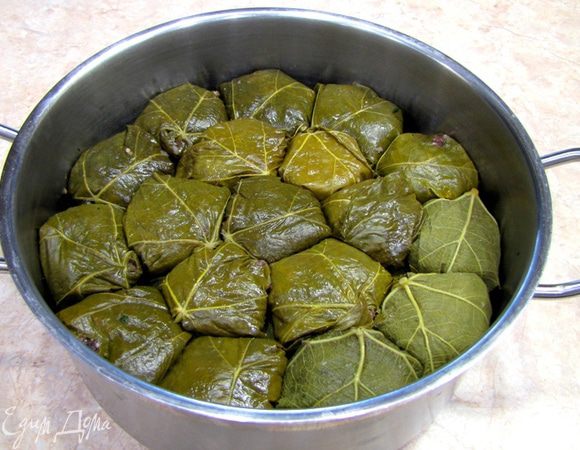 Положите один лист на ладонь шершавой стороной вверх (так при заворачивании торчащий стебелек от листа спрячется внутрь) сверху у основания листа положите 40-50 грамм фарша. Заворачивайте лист наверх. Я кладу много фарша и снизу лист не заворачивается дважды. Укладывайте в низкую широкую кастрюлю сложенной частью вниз. Укладывайте плотно, чтобы не было расстояний.
У меня получилось три слоя.