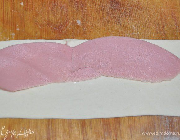 Колбасу разрезать на полоски и положить полосочку колбаски на тесто.