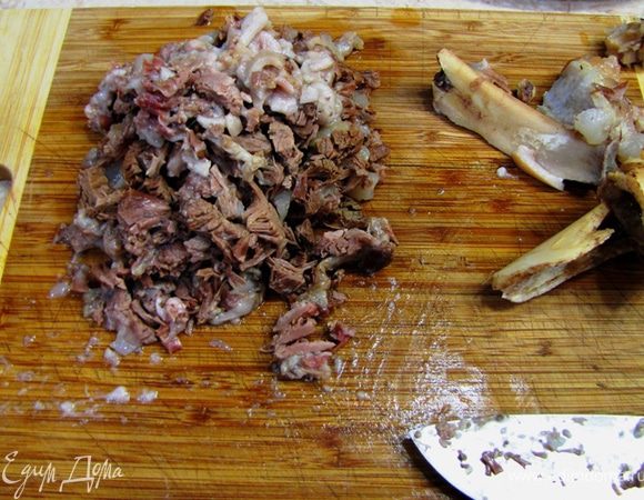 Дайте мясу остыть до температуры, при которой вы сможете с ним работать (горячее, но не обжигающее). Выберите из мяса, кожи и хрящей все косточки очень тщательно. Мясо будет разваливаться. Прощупайте его все, чтобы ни одна косточка не осталась и ваши гости не потеряли свои зубы. Для этого берите небольшие кусочки и прощупывайте пальцами, иначе все равно пропустите. Мясо с кожей, жиром и пр. порежьте на кубики в пол сантиметра (не старайтесь особо, все равно и мясо и кожа будут очень нежными и вкусными). Мясо режьте поперек волокон очень острым ножом, так как оно разваливается.