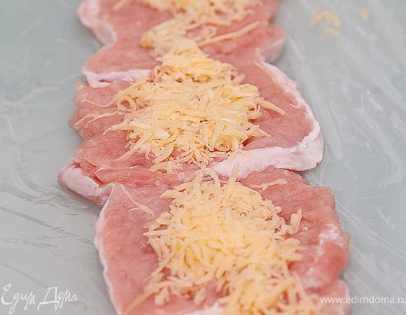 Рабочую поверхность застилаем пищевой пленкой, размер которой не меньше полуметра в длину. Излишки коньяка пропитываем салфеткой. На пленку укладываем внахлест мясные отбивные.
Натираем сыр и чеснок на мелкой терке и смешиваем с майонезом.  Эту сырную смесь аккуратно наносим поверх мяса. На края стараемся особенно не заходить, лучше ближе у центру.