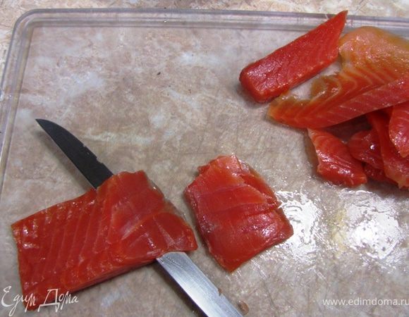 Найдите в филе место, где находятся кости, это ряд, толщиной около 5 мм посередине толстой части филе. Удалите кости с помощью пинцета.
Отрежьте толстую часть филе и срежьте все тонкие части с него. У вас в итоге должен получиться брусок толщиной около пяти сантиметров.
Нарежьте этот брусок поперек под углом толщиной около трех миллиметров. У вас получится 25-30 ровных тонких кусочков.
Оставшиеся обезки, а также тонкую часть филе нарежьте небольшими полосками для ролов. Примерно половину полосок я порезал на кубики для Гунканмаки.