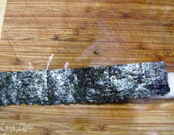 Приготовление Гунканмаки
Намочите руки в воде, смешанной с небольшим количеством уксуса.
Слепите небольшой овал из риса диной 4 и шириной 2 сантиметров.
Приложите полоску нори, как показано на фотографии. Помните, что при заворачивании полоски нори, рис должен оказаться с одной стороны (точнее он будет снизу), а с другой стороны вы будете закладывать начинку.