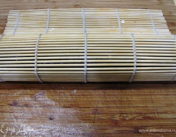 Придерживая пальцами начинку начните заворачивать ролл вместе с бамбуковым ковриком. Как только вы сделаете один оборот, сразу высвобождайте бамбуковый коврик, чтобы он не завернулся внутрь ролла.