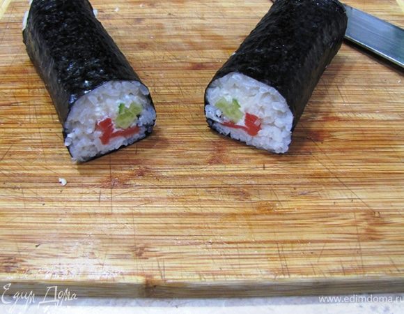 Возьмите острый нож. Смочите его в воде с уксусом.
Разрежьте ролл поперек точно посередине. Японцы это делают резким рубящим движением вниз. Лично у меня лучше получаются аккуратные пилящие движения.
Если ролл получился у вас плотным, то проблем с ровным разрезанием быть не должно.