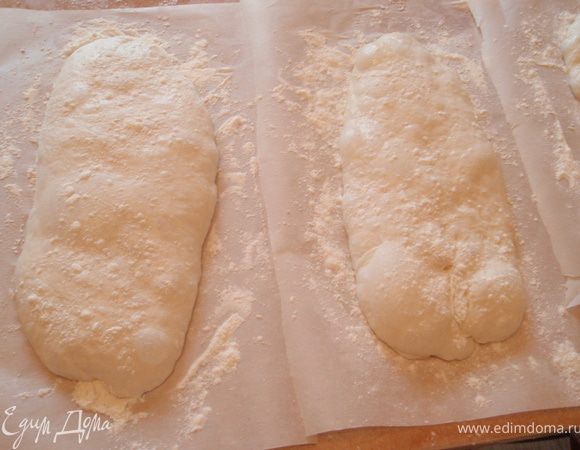 С помощью двух шпателей подхватить чиабатту с двух концов и перенести каждую на отдельный посыпанный мукой кусок бумаги.Подержать так 1 часЗатем осторожно вместе с бумагой переложить или даже перетащить чиабатту на подогретый протвинь и печь при температуре250 градусов 15 минут,пока она не станет слегка коричневатого цвета.Остудить на решетке