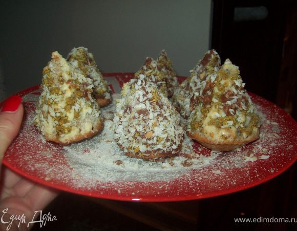 На бумаге для выпечки нарисуйте круги диаметром 20 см, вырежьте их, разрежьте до середины, сверните кулечки и закрепите скрепками. Бумажные кулечки поставьте вертикально,например, в стаканы диаметром меньше, чем диаметр кулечков.
Белки отделенные от желтков взбейте с щепоткой соли до устойчивой пены. Продолжайте взбивать, добавляя сахар.Затем добавьте желтки.Молотый миндаль смешать с мукой и крахмалом. Аккуратно вмешать мучную смесь в яичную массу.Тестом наполнить кулечки.Печь в предварительно нагретой до 180°C духовке минут 15-20. Вынуть из духовки и дать остыть.Фисташки подробить.Белый шоколад растопить на водяной бане.Остывшие бисквиты освободить от бумаги.Бисквиты обмазать шоколадом и обвалять в дробленых фисташках.Красные точечки-шарики (любое варенье)нанести можно при помощи обычного шприца без иглы.Сахарную пудру смешать с лимонным соком и чайной ложкой полить деревца.Посыпать сверху все сахарной пудрой