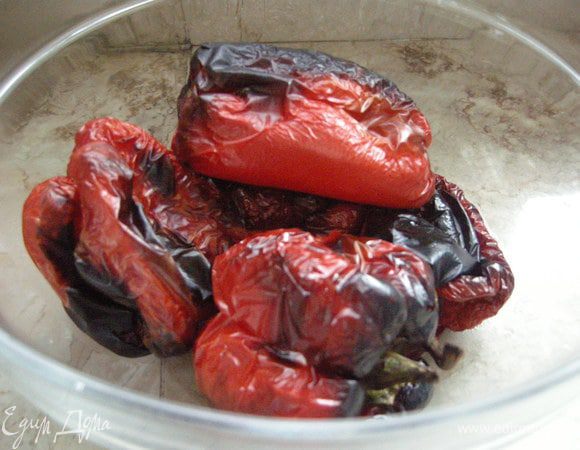 Включить гриль и печь перцы до образования черной корки. Вынуть из духовки и перенести в стекляную посуду, накрыть пленкой и дать остыть.