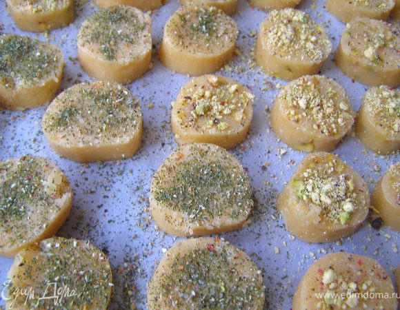 Холодное тесто нарезать кружками толщиной 1 см. Выложить печенье на лист, покрытый бумагой для выпечки. Смазать верх белком.
Печенье БЕЗ фисташек посыпать смесью перцев и травами, остальное - измельчёнными фисташками.
