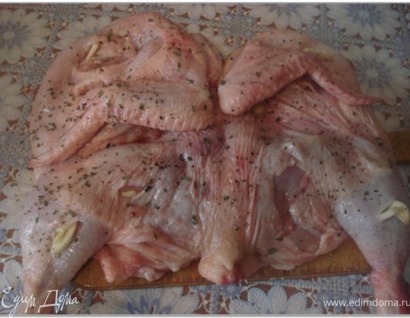 Цыпленка тщательно вымыть, обсушить и при необходимости обпалить. Положить цыпленка на разделочную доску и осторожно разрезать вдоль грудки. Чеснок очистить. 2 зубчика чеснока разрезать примерно на 10 тонких долек. Остальной чеснок мелко нарубить или пропустить через ручной пресс. Цыпленка хорошо отбить с обеих сторон, натереть солью, молотым красным и черным перцем. Сделать на коже небольшие надрезы и нашпиговать их дольками чеснока.