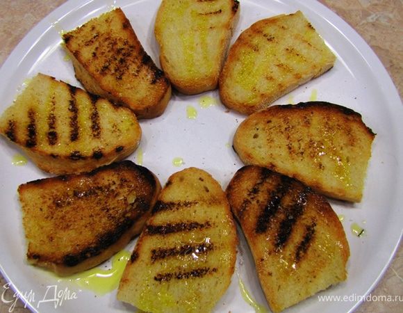 Сложите кростини на блюдо и полейте оливковым маслом (чуть-чуть. как раз хватит столовой ложки. Не старайтесь попасть равномерно. Масло великолепно передаст вкус хлебу). Непного посолите и поперчите.