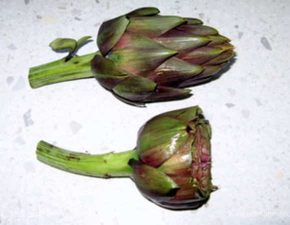 Сначала артишоки нужно правильно почистить.Это совсем не сложно, но советую вам приготовить перчатки, потому что они сильно и неприятно пачкают кожу рук. Ещё нужно приготовить миску. Алюминиевую и металлическую посуду для приготовления артишоков лучше не использовать , поскольку артишоки в такой посуде чернеют. В миску надо налить воды и выжать лимон, тогда артишоки сохранят свой цвет и не потемнеют.
Первый шаг: нужно отрезать стебель, оставив только 10 см от места, в котором он переходит в цветок.
Второй шаг: нужно отсечь верхнюю часть бутона, примерно, на 1/3. На фотографии видно, каким он был и каким стал.
