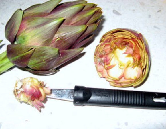 Четвёртый шаг: нужно удалить центральную часть бутона. Она непритяна на вкус и похожа на солому. Если вы не планируете фаршировать артишоки, то их для этого можно разрезать пополам, и вы сразу увидите внутри волокнистую сердцевину.В зависимости от сорта, её бывает больше или меньше. Удалите её. Если же вы собиратесь фаршировать артишоки, лучше использовать чайную ложечку или специальное приспособление, чтобы не повредить целостность цветка.