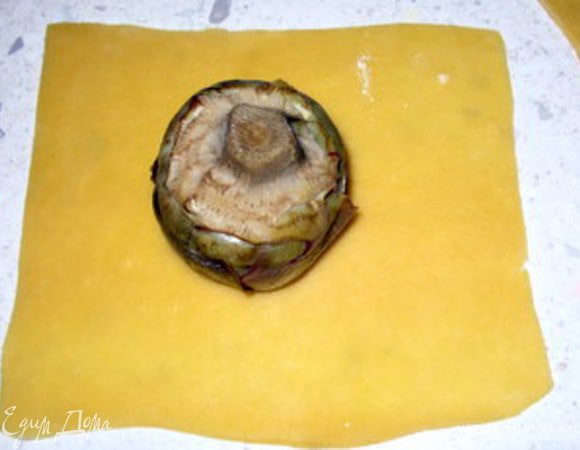 Приготовить начинку. Для первого варианта перемолоть в блендере ветчину и смешать её с сыром, посолить,поперчить. Для второго варианта снять шкурку с колбасок, раскрошить их и обжарить пару минут на оливковом масле. Наполнить артишоки начинкой.
Раскатать тесто в тонкий пласт и нарезать на 6 квадратов, подходящий по размеру для того, чтобы в них завернуть артишок. 
Разместить по центру квадрата артишок начинкой вниз и соединить углы теста, чтобы получился «узелок». 
