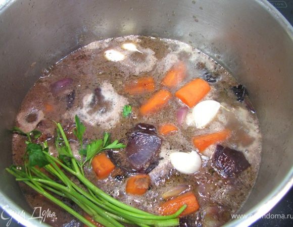 Кладем обратно овощи в мясо, заливаем маринадом, бульоном и четырьмя ложками коньяка.
Кладем травы, чеснок.