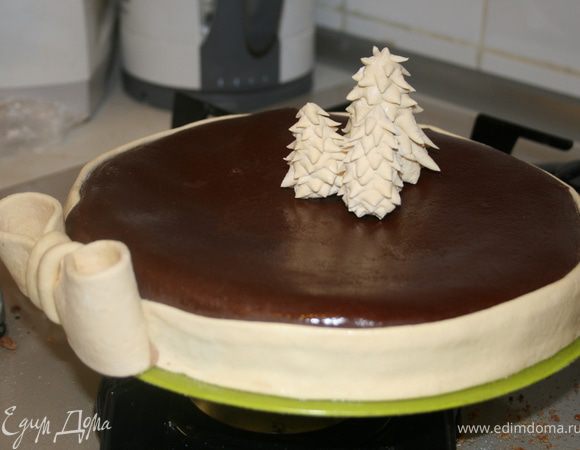 Раскатать шоколадную мастику, покрыть торт и украсить елочками и бантом. Если на мастике останется пудра смазать эти места водкой при помощи кулинарной кисти.