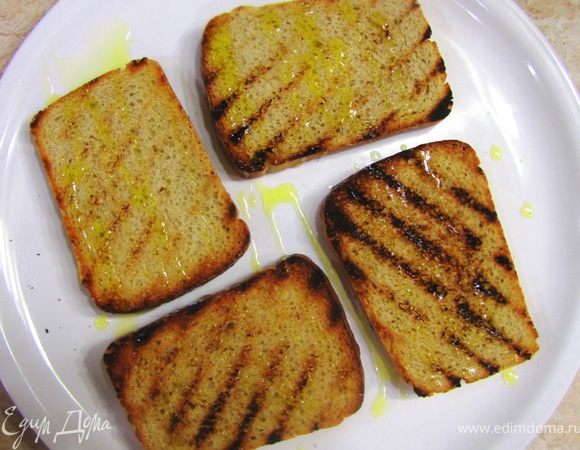 Перекладываем ломтики на тарелку и чуть остывшие натираем чесноком (не очень сильно).
Посыпаем солью и перцем и сбрызгиваем оливковым маслом. Очень важно, чтобы масло было первого отжима (Extra Virgin), так как оно используется здесь для запаха и вкуса.