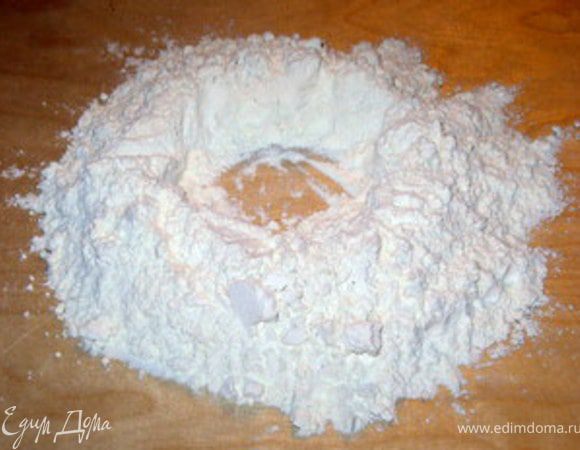 Замесить тесто.Для этого высыпать муку горочкой на деревянную рабочую поверхность.
В центре сделать углубление.