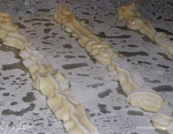 Из части массы теста сделаем маленькие бисквитные печенья (их количество зависит от предполагаемых кусков торта). Из оставшейся части массы изготовим бисквитные полоски. Для этого выдавим на противень, выложенный бумагой для выпечки, полоски в длину противня. Посыпем сахарной пудрой. 