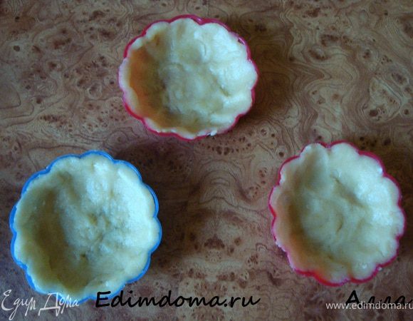 Замесить тесто, дать ему полежать в холодильнике минимум 30 минут, а лучше 2 часа. Разделить на кусочки и распределить по тарталеткам, хорошо прижимая тесто по краям и дну, формируя небольшое углубление по центру. Если формочки силиконовые смазывать из не нужно, а если металлические, то смажьте их. Заполненные формочки поставьте в холодильник.