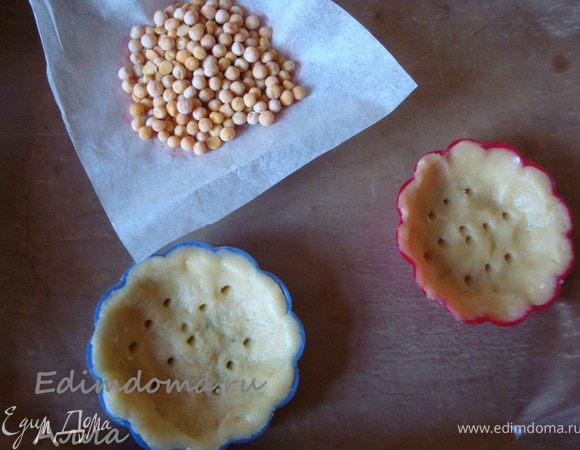 Разогреть духовку до 180 градусов. Вынуть тарталетки из холодильника, в нескольких местах проколоть тесто, накрыть кусочками бумаги для выпечки и прижать горохом. Отправить тарталетки в духовку минут на 20.