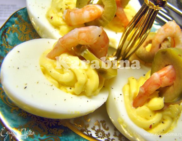 Яйца разрезаем пополам. Аккуратно вынимаем желток. Отдельно смешиваем желток с майонезом и горчицей (ориентируйтесь на Ваш вкус). С помощью кулинарного шприца (или просто ложкой) заполните белок начинкой. Оливки нарежьте кольцами. В каждое колечко просуньте креветку и украсьте фаршированное яйцо. 