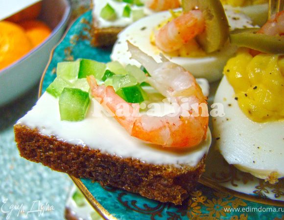 Хлеб нарежьте квадратиками. Каждый кусочек смажьте сливочным сыром. Затем посыпьте нарезанным на мелкие кубики огурцом и украсьте креветкой. 
