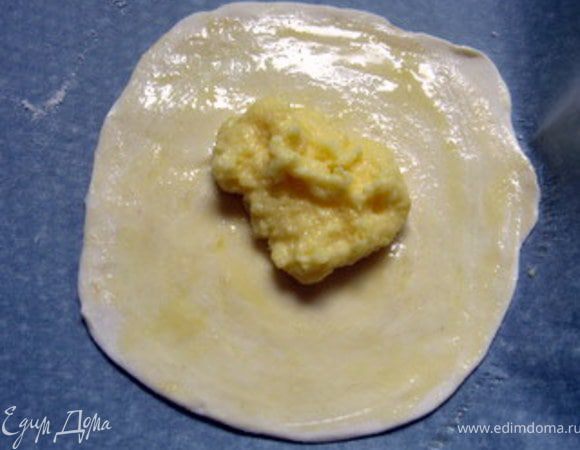 Приготовить противень, накрыть его пергаментом. Разогреть духовку до 180° .
Раскатанный диск перенести на противень, смазать его взбитым яйцом и выложить в центр около чайной ложки крема. 