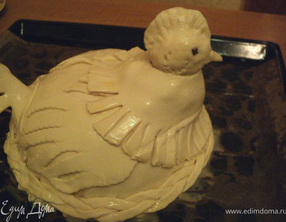 Установить шейку на пирог. Для большей устойчивости прикрепить шейку к пирогу, проткнув ее деревянной шпажкой. Из теста скатать головку и прикрепить ее к шейке, насадив на шпажку. Из теста также вырезать крылья и хвостик. Крылья прикрепить к пирогу, смазав его взбитым яйцом, хвостик закрепить с помощью зубочисток ( убрать после выпечки пирога).