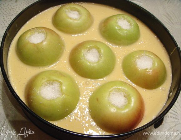 Выложить яблоки в глубокую форму для запекания, смазанную маслом. Между яблоками залить тесто. Выпекать в духовке 50 мин при 180℃.  