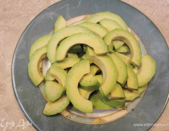 Разрежьте авокадо вокруг косточки, поверните половинки авокадо так, чтобы одна из половинок отделилась от косточки. Ударьте ножом по косточке, чтобы нож вонзился в нее. Поверните нож так, чтобы косточка отделилась от второй половинки авокадо. Если у вас спелый авокадо, то вы легко столовой ложкой вытащите половинки плодов из кожуры. Нарежьте половинки на полукольца.