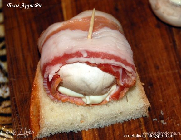 Получившийся рулетик положить на хлеб шляпкой вниз, чтобы, вытекая, сыр попадал на кусочек хлеба. Закуску зафиксировать зубочисткой.