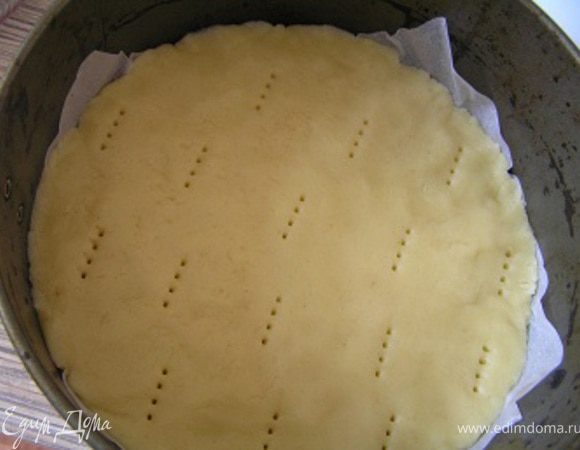 Форму для выпечки застелить пекарской бумагой, распределить тесто, проколоть вилкой в нескольких местах.