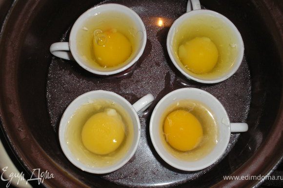 Готовим яйца. Для этого берем маленькие чашечки (у меня кофейные), смазываем их сливоным маслом и вливаем в них яйцо. Чашечки ставим в кастрюлю с кипятком и варим их таким образом до готовности.