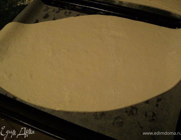 Из размороженного пласта слоеного теста вырезать овал. Перенести его на противень, застеленный бумагой для выпечки.