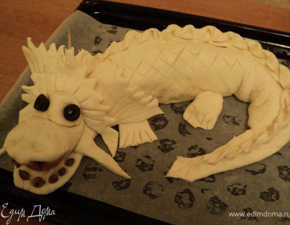 По телу дракона сделать ножом косые насечки, смазать пирог взбитым яйцом, посыпать семенами кунжута. Выпекать при температуре 180 градусов 1 час.  В местах, где пирог начнет сильно румяниться, прикрыть фольгой.