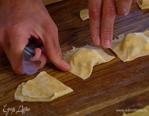 На одну половину теста поместить начинку, выкладывая ее горками по пол чайной ложки на некотором расстоянии друг от друга, накрыть второй половиной теста, влажными руками скрепить края и ножом разрезать тесто на квадратики с начинкой посередине. Если края у равиоли расходятся, скрепить их вручную.