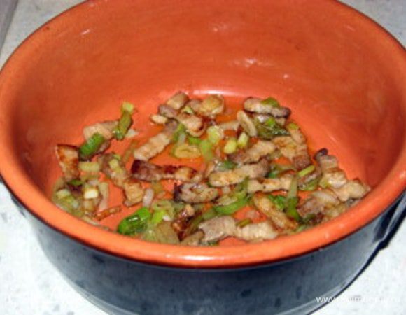 Приготовить глиняный горшочек. Его лучше замочить в воде за час до использования.Выложить на дно половину грудинки с луком.