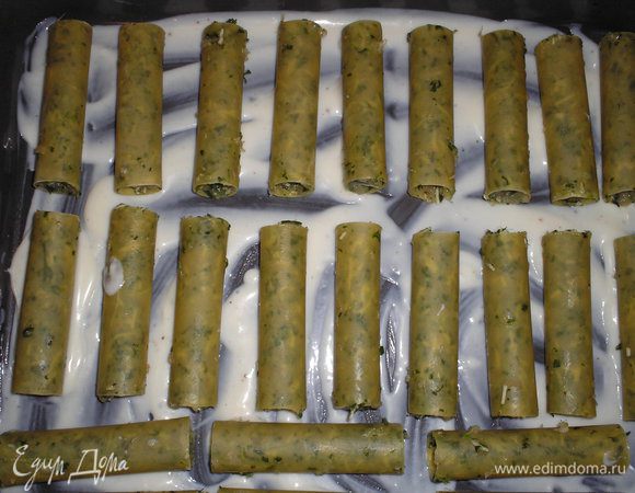 На противень наливаем несколько ложек соуса, равномерно распределяем. Выкладываем каннелони на растоянии друг от друга 2-3 см(для этого я беру большой противень, потому что несколько раз укладывала в два шара и потом каннелони ужасно слипались друг с другом). 