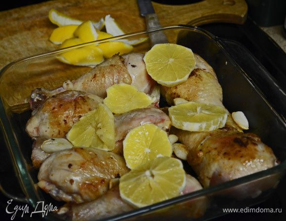 В большой сковороде разогреть сливочное и оливковое масло. Обжарить окорочка со всех сторон до золотистого цвета. В конце процесса добавить целые зубчики чеснока и немного их обжарить. Обжаренные окорочка положить в огнеупорную посуду, равномерно разложить чеснок и кружки лимона.