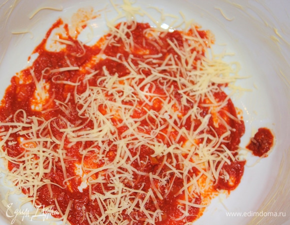 Смазываем керамическую форму кусочком сливочного масла. На дно формы выкладываем немного томатного соуса, сверху присыпаем тертым сыром.