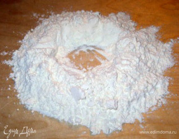Замесить тесто.Для этого высыпать муку горочкой на деревянную рабочую поверхность.
В центре сделать углубление.