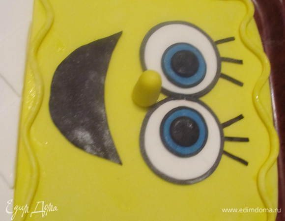 Скатать из желтой мастики жгутик и волнисто положить по приметру головы. Из жгутика потолще сделать носик. Из черной мастики вырезать ротик и также подчеркнуть черной полоской. 