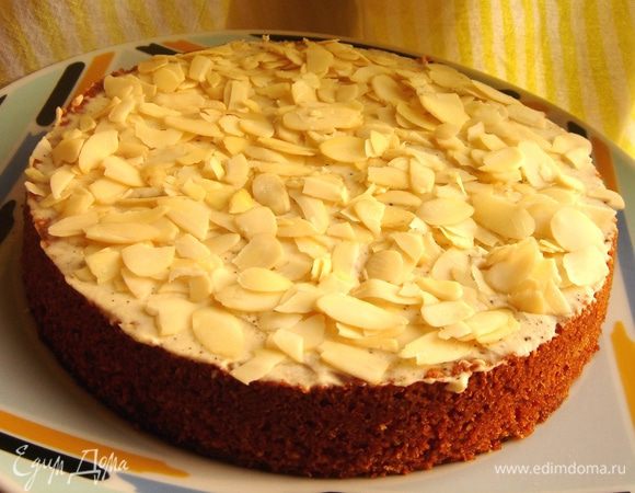 Сливочное масло комнатной температуры немного взбить. Затем добавить охлаждённый творожный сыр, сахарную пудру и ванильную эссенцию. Взбить до однородности. Поверхность кекса смазать кремом и обсыпать миндальными лепестками. Приятного чаепития!