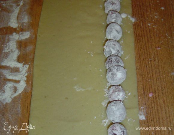 Тесто раскатываем и нарезаем полосками шириной 7 см. На край полосок выкладываем вишни,