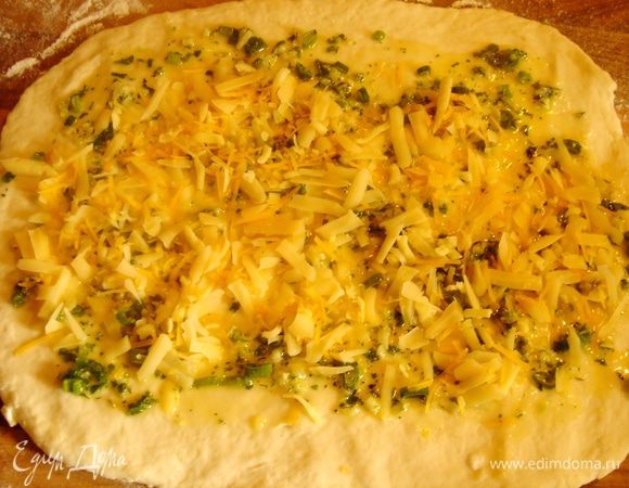 Для приготовления начинки растопить сливочное масло и смешать его с мелко рубленной травой и раздавленным чесноком.Посолить.Разделить тесто на две части и раскатать каждую  в прямоугольник толщиной не более 0,5 см.Щедро смазать тесто масляной смесью и присыпать сыром.