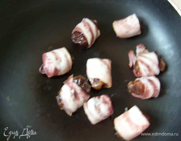 Нарезать бекон полосками, обернуть каждый финик и поджарить на сковороде без добавления масла несколько минут. 