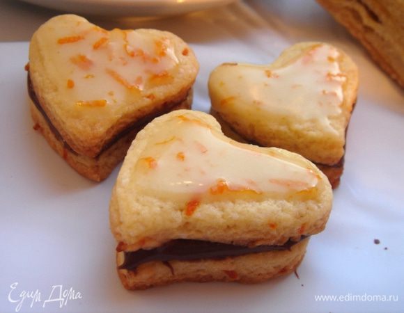 Для песочного печенья взбейте масло с сахаром,добавьте яйцо и цедру.Смешайте муку,соль и ванилин.Соедините обе смеси и вымесите мягкое,нелипкое тесто.Раскатайте на присыпанной мукой поверхности в пласт,толщиной 3 мм.Вырежьте сердечки формочкой,выложите их на противень с пергаментом и уберите противень в холодильник на 20 минут.Охлаждённые  печенья выпекайте при 180*С минут 10,когда печенье чуть-чуть начнёт румянится.Охладите печенье,соедините их по два с помощью Нутеллы.Смешайте сахарную пудру с цедрой  и небольшими порциями добавьте сок.Полейте глазурью печенье.